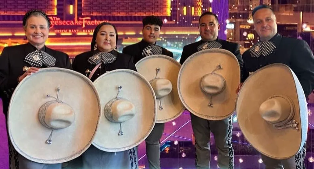 Cinco integrantes del mariachi con traje de charro negro sostienen sus sombreros de ala ancha frente a la cámara