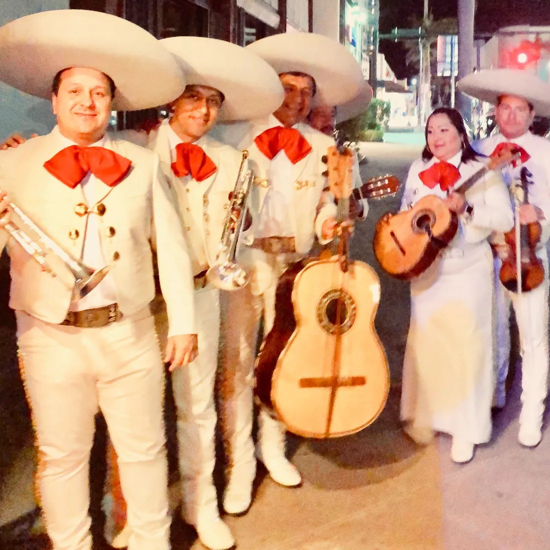 Mariachi con traje blanco y moño rojo de noche
