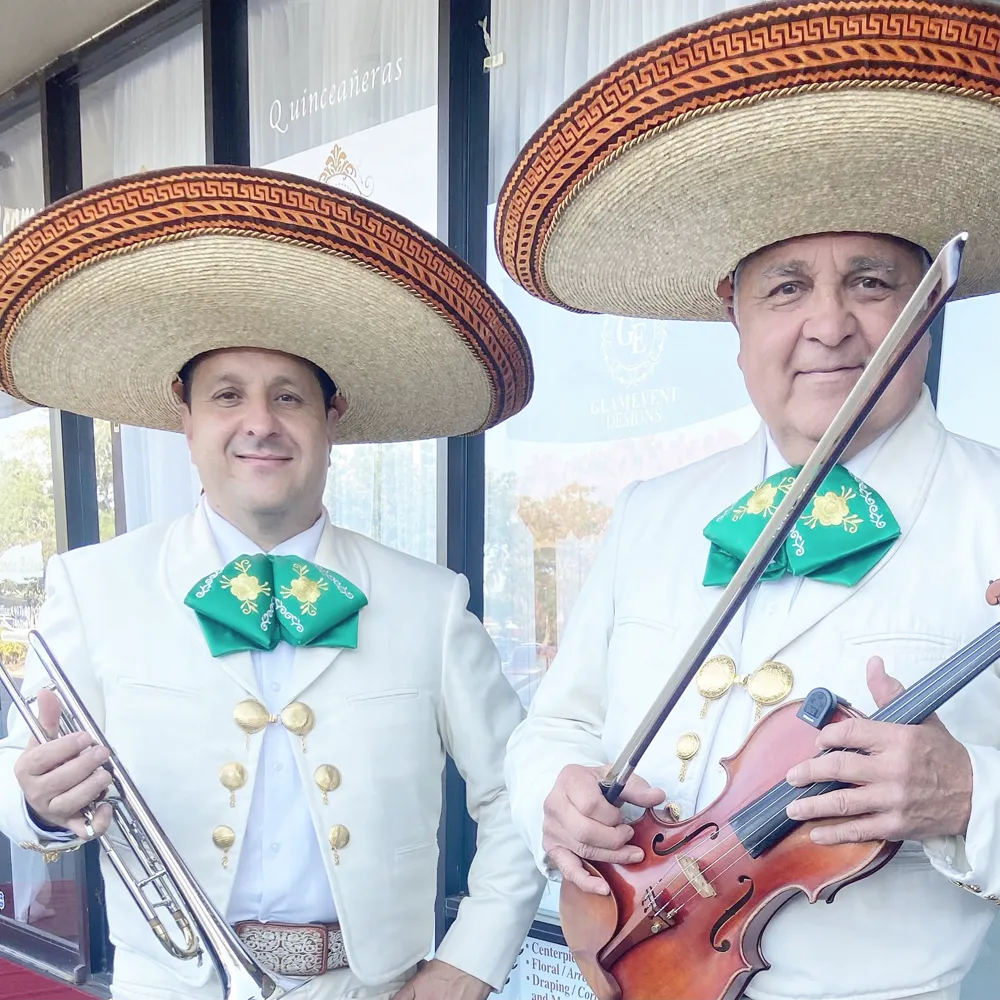 Dos músicos del mariachi con traje blanco, moño verde y sombrero de ala ancha, uno con la trompeta y otro con el violín y el arco
